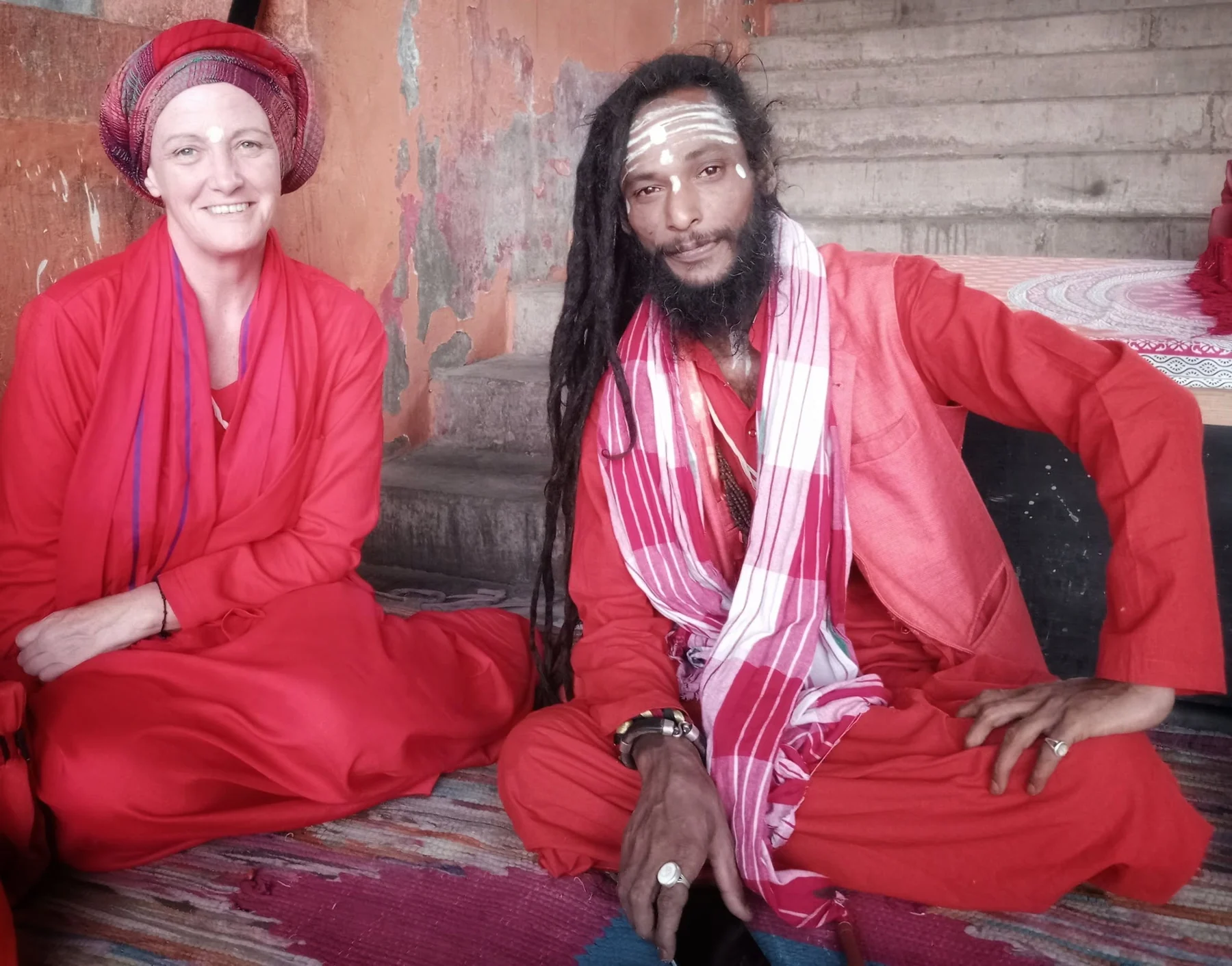 Two people in red clothing seated together by a wall